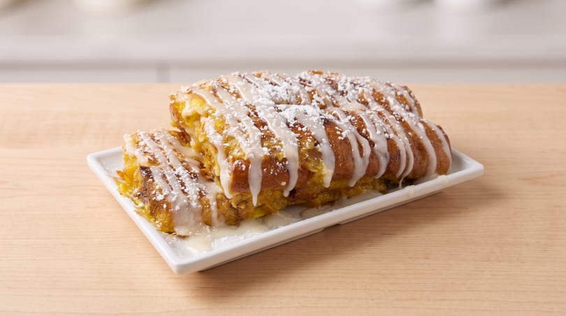 Golden French toast covered in white icing and powdered sugar on a white plate.