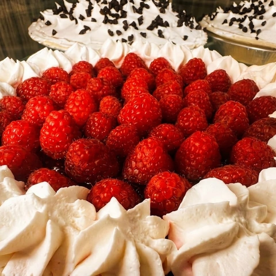 Close-up of a raspberry pie with whipped cream, with other pies in the background.