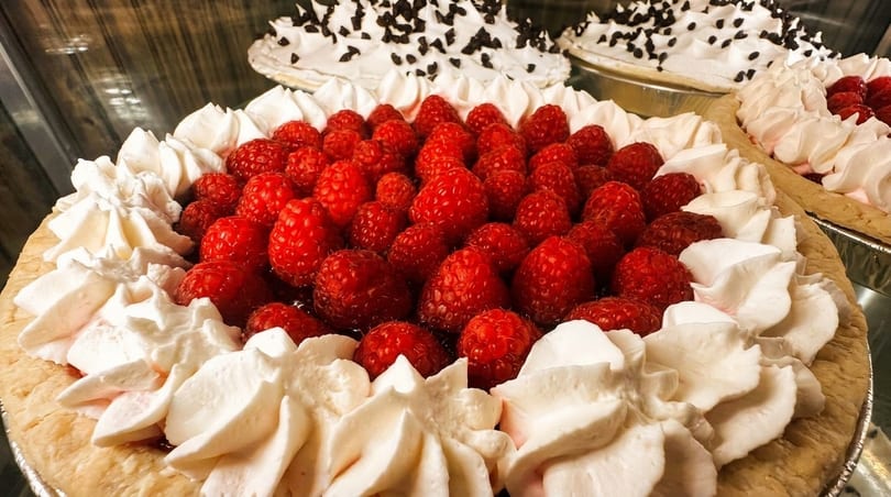 Close-up of a raspberry pie with whipped cream, with other pies in the background.